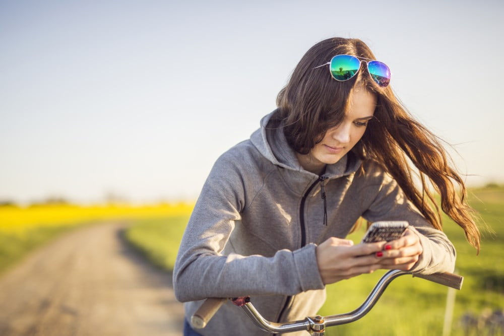Ung dame med sykkel som har stoppet og taser på mobilen