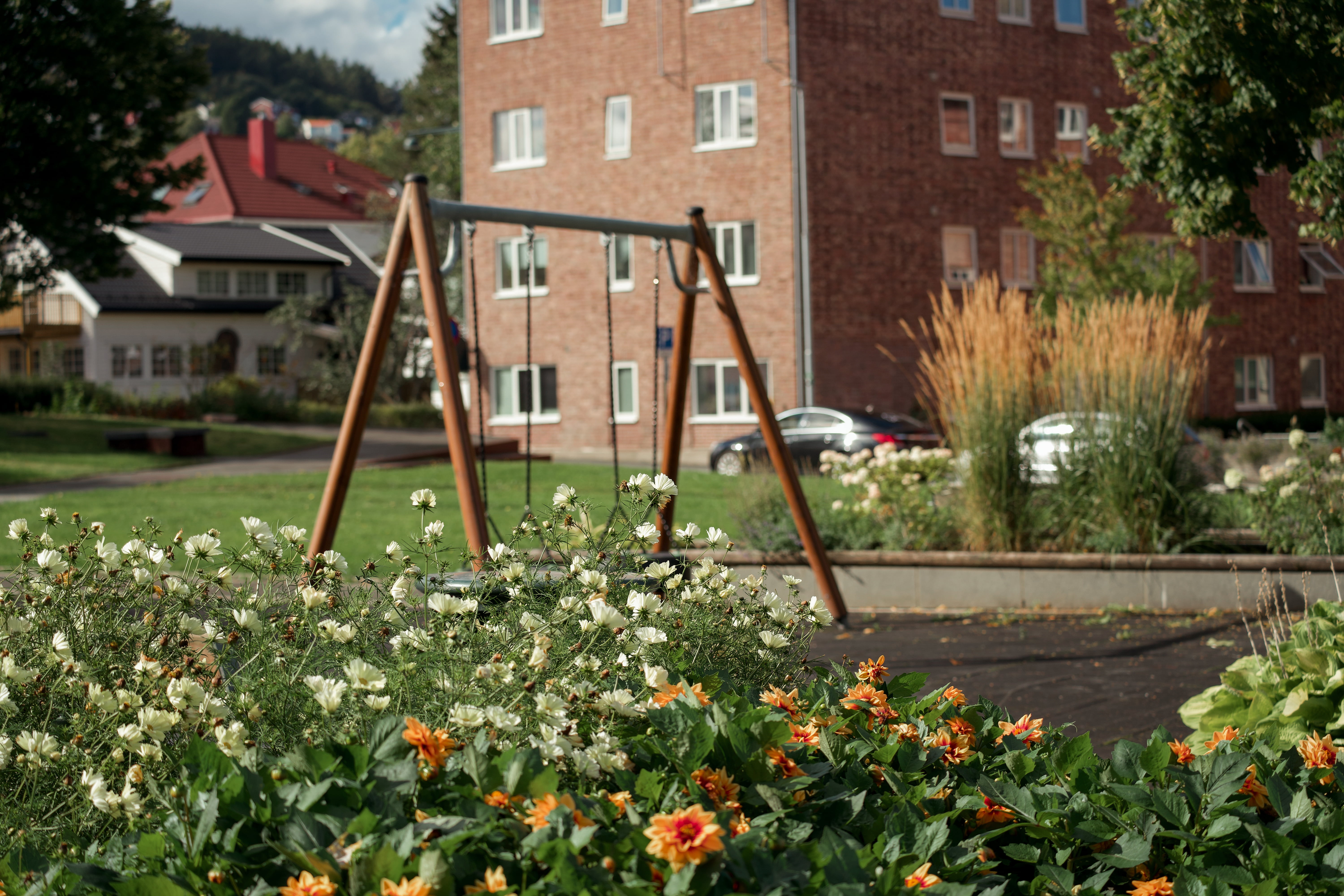 Blomsterbed og husker i en grønn felles hage foran en rød murbygning i et borettslag.