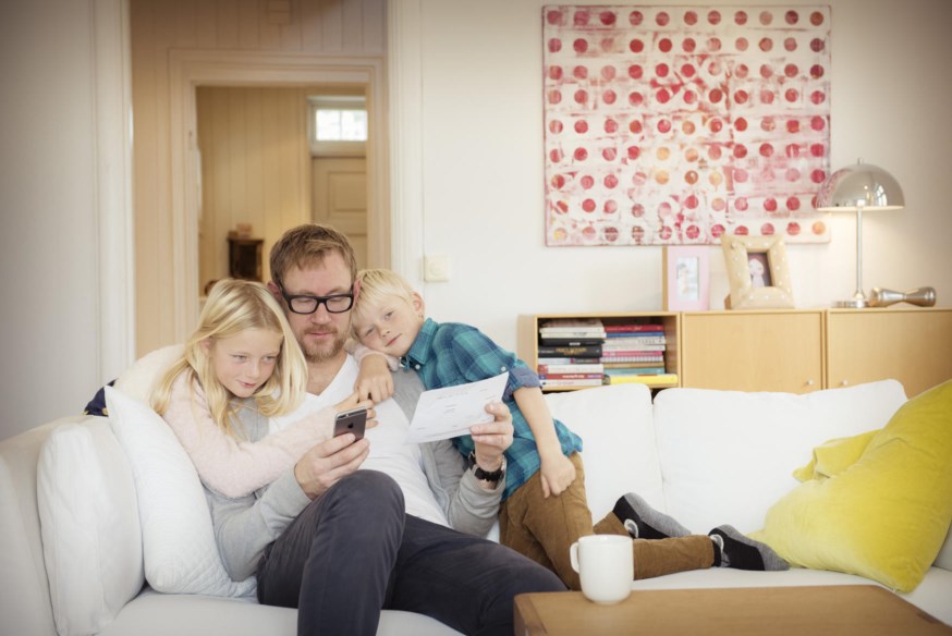 Far og barn ser på nettbrett i sofaen. foto